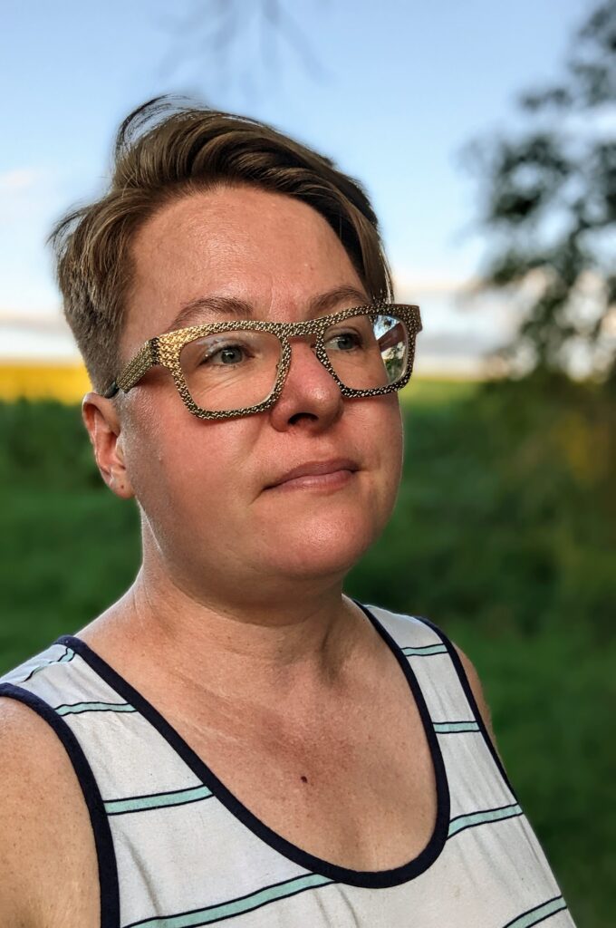 Tara in a field, wearing gold glasses and a white tank top